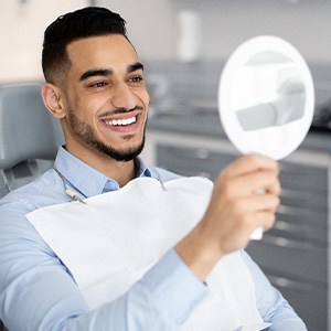 Man smiling at reflection in handheld mirror
