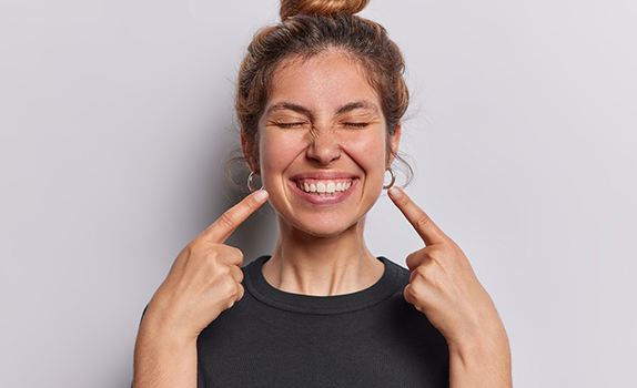 a woman pointing to her smile   