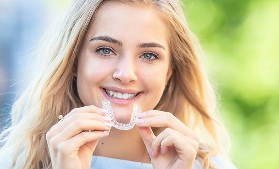Woman with blond hair smiling while holding ClearCorrect aligner