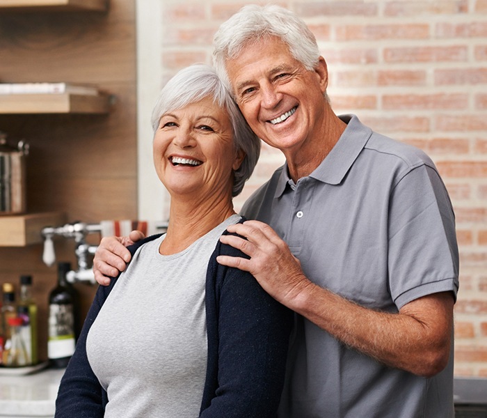 Man and woman smiling after full arch treatment