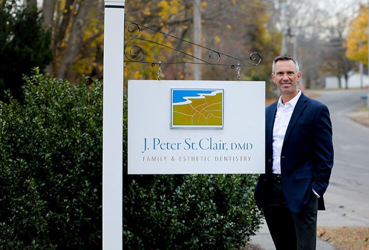 Doctor Saint Clair standing next to dental office sign