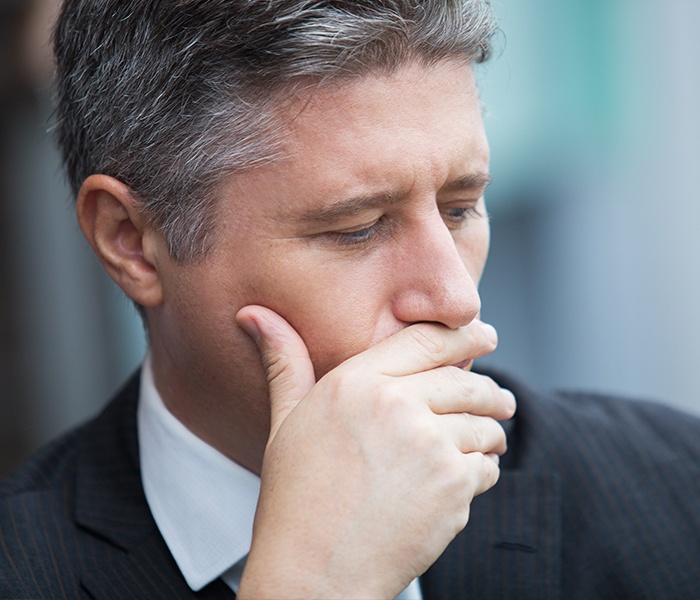 Man suffering consequences of gum disease covering his mouth 