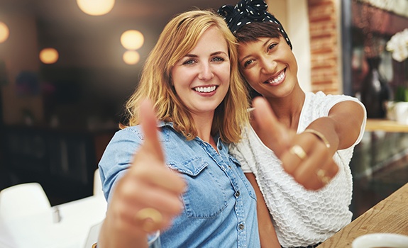 Two women giving thumbs up after porcelain veneer treatment