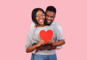 young couple in gray sweaters holding red heart 